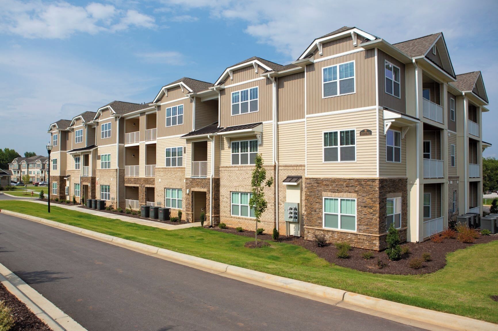 A multi-story apartment building with a brick facade, multiple balconies, and a well-maintained lawn.