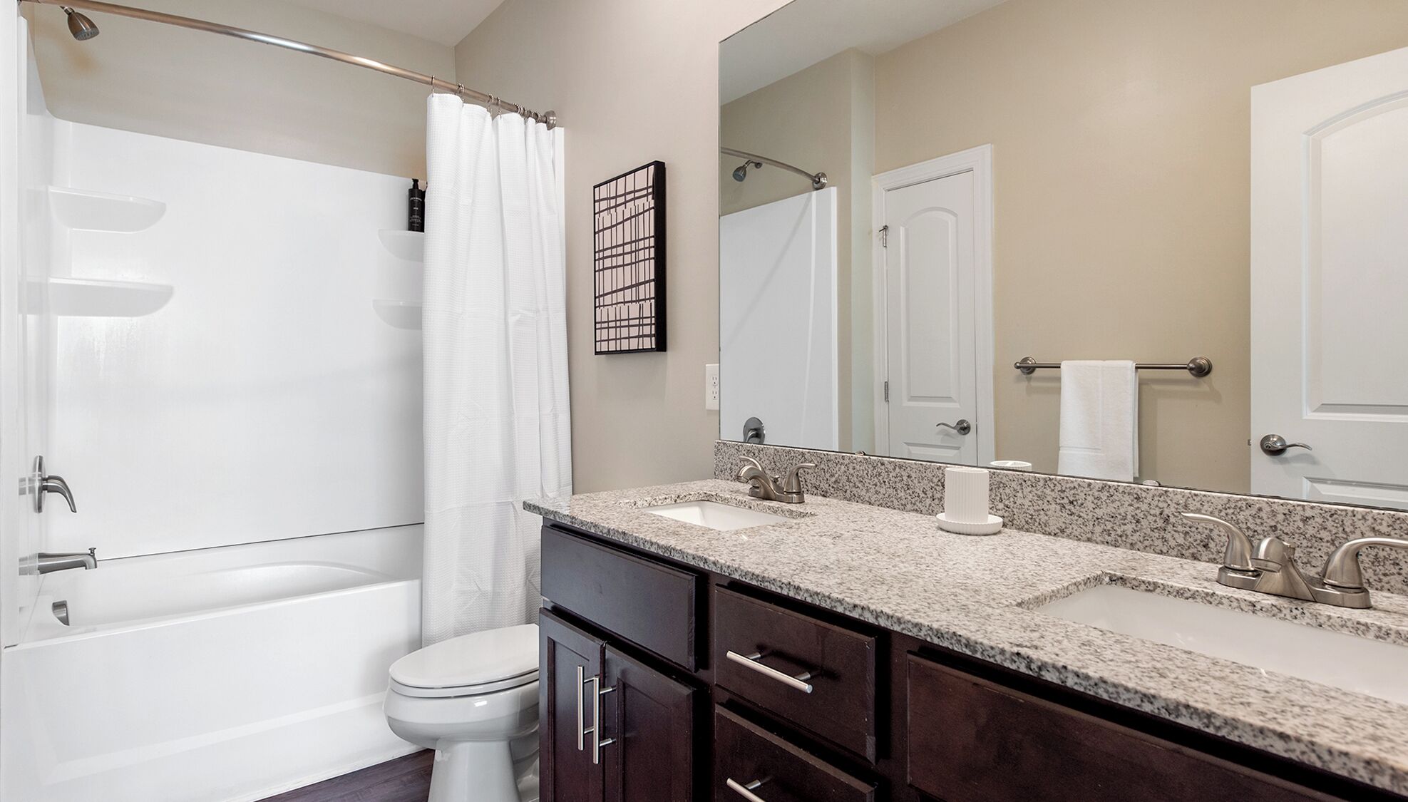 A modern bathroom with a bathtub, a toilet, a double sink vanity, and a large mirror.