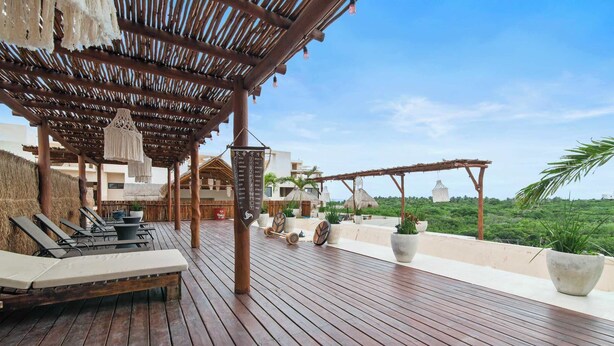 A wooden deck with lounge chairs, a pergola, and potted plants. - Penthouse with Rooftop Plunge Pool - Distant Ocean (Tulum)