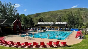 Ein Schwimmbecken mit mehreren Bahnen, roten Liegestühlen und einem Gebäude mit roter Fassade.
