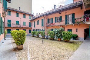 A courtyard with a cobblestone ground, potted plants, and buildings with balconies. - GuestHost - CASA ACQUA&CIELO (Milan)