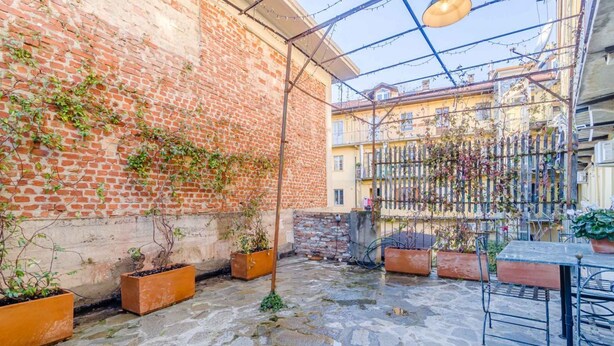 Ein Innenhof mit Ziegelmauern, Blumentöpfen, einem Metalltisch und Stühlen.