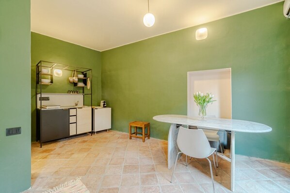 A modern kitchen with a white countertop, a wooden stool, and a dining table with chairs.