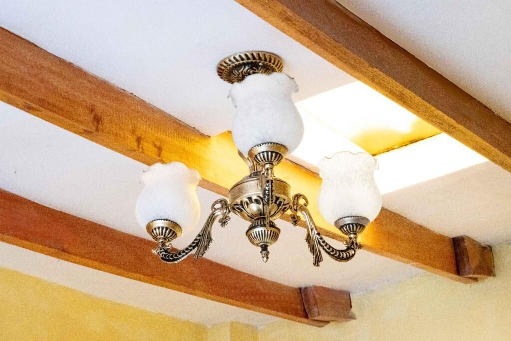 Un candelabro con tres globos blancos y estructura metálica, colgado del techo de vigas de madera.