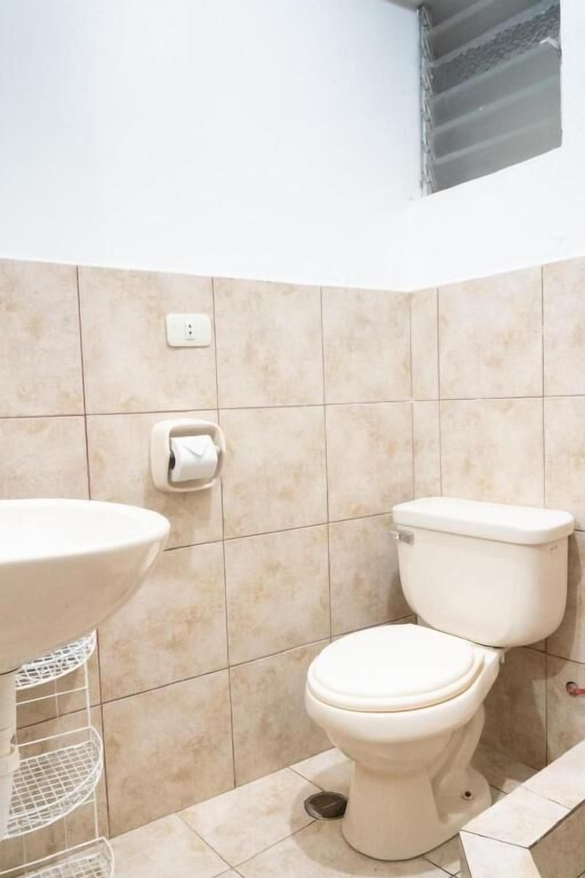 Een badkamer met toilet, wastafel en een rol toiletpapier aan de muur.
