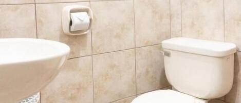 Een badkamer met toilet, wastafel en een rol toiletpapier aan de muur.