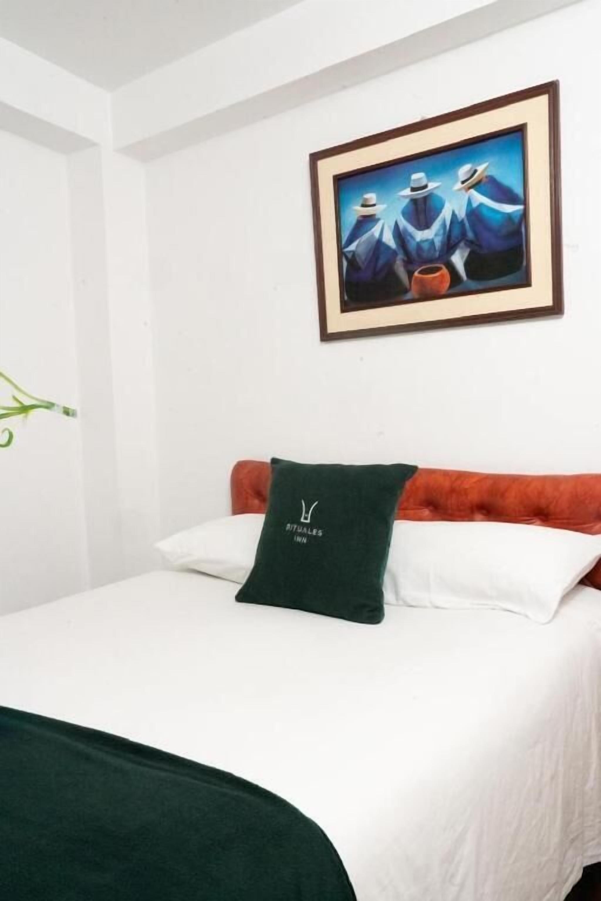 A hotel room with a bed, white walls, a framed painting, and a green pillow.