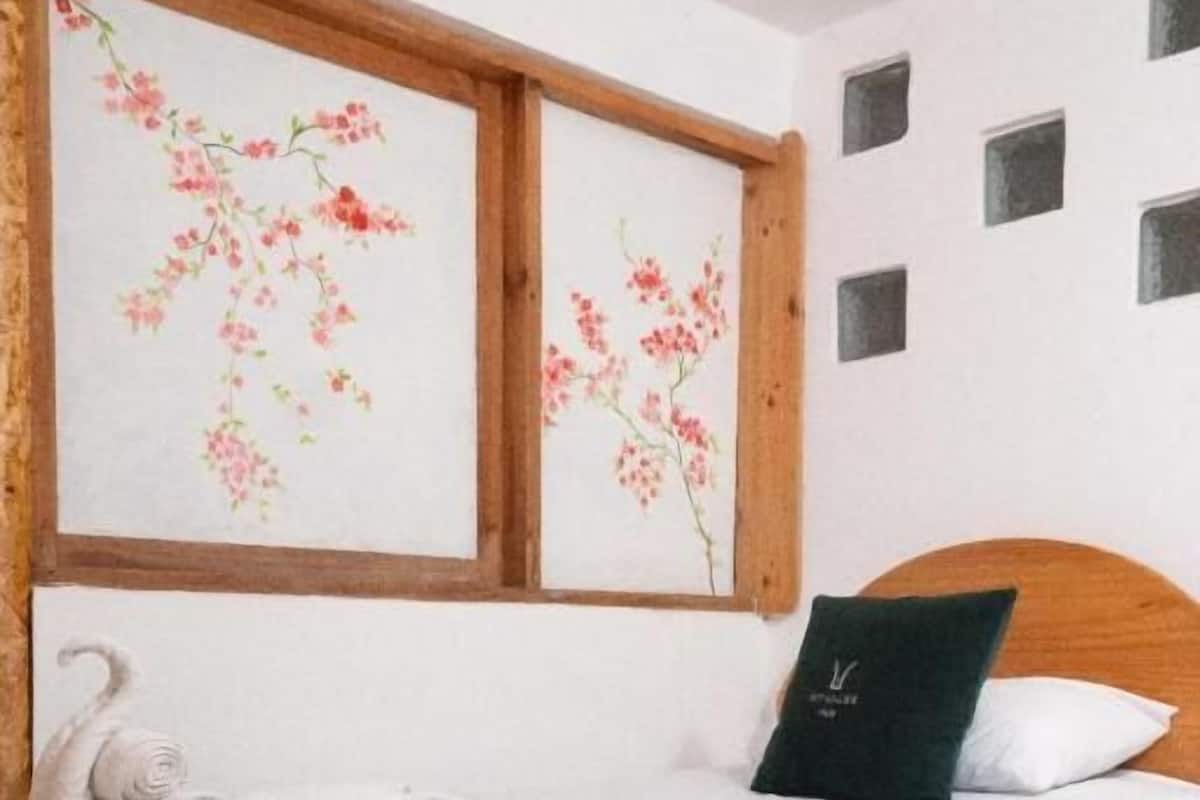 A neatly made bed with a green throw blanket, a white pillow with a logo, and a decorative swan towel.