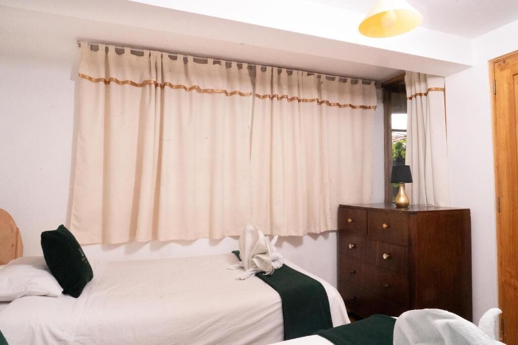 A hotel room with a bed, a wooden dresser, a lamp, and a window with curtains.