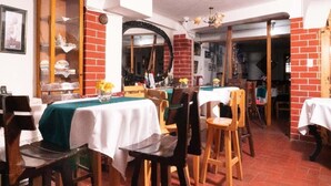 A dining area with brick walls, wooden furniture, and a large mirror. - Rituales Inn Santa Monica  (Cusco)