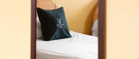 Un dormitorio con una cama, un almohadón con logotipo y una pared decorada con motivos florales.