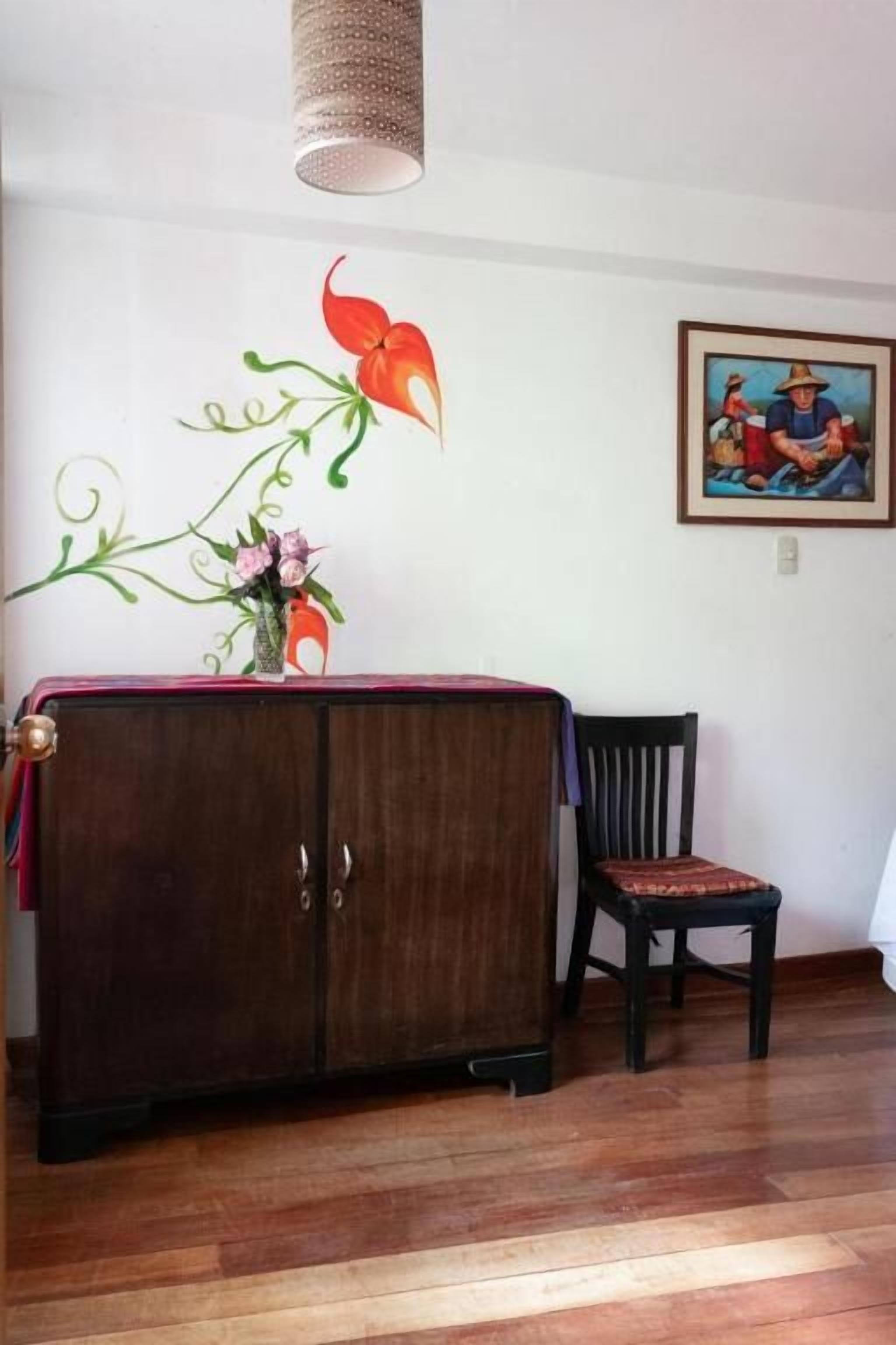 Una habitación con un armario de madera, una silla, un muro con un adhesivo floral y una lámpara colgante.