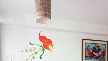 Una habitación con un armario de madera, una silla, un muro con un adhesivo floral y una lámpara colgante.