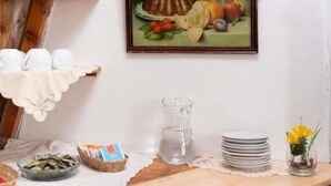 A wooden shelf with pottery, a painting of fruits and flowers, and a table with plates and a vase. - Rituales Inn Santa Monica  (Cusco)