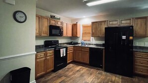 A kitchen with wooden cabinets, a black refrigerator, a microwave, and a stove. - Charming 2-bedroom lakehouse with HVAC in cozy Roxboro (Roxboro)