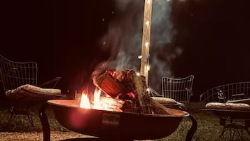 Una scena esterna notturna con un braciere, luci a catena e sedie.