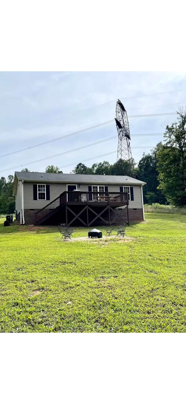A single-story house with a porch, a small lawn, and a tall power line tower in the background. - Charming 2-bedroom lakehouse with HVAC in cozy Roxboro (Roxboro)