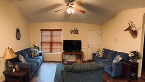 A living room with two sofas, a ceiling fan, a mounted deer head, and a television. - Charming 2-bedroom lakehouse with HVAC in cozy Roxboro (Roxboro)