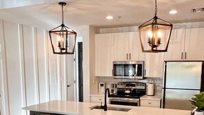 Una cocina moderna con una isla central, electrodomésticos de acero inoxidable e iluminación colgante.