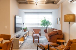 A modern living room with a sofa, chairs, a TV, a plant, and a lamp. - Leblon | 3 Quartos, 2 min da Praia - por Casapē Rio (Rio de Janeiro)