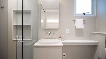 Un baño moderno con cabina de ducha de vidrio, un lavamanos blanco y un espejo encima.