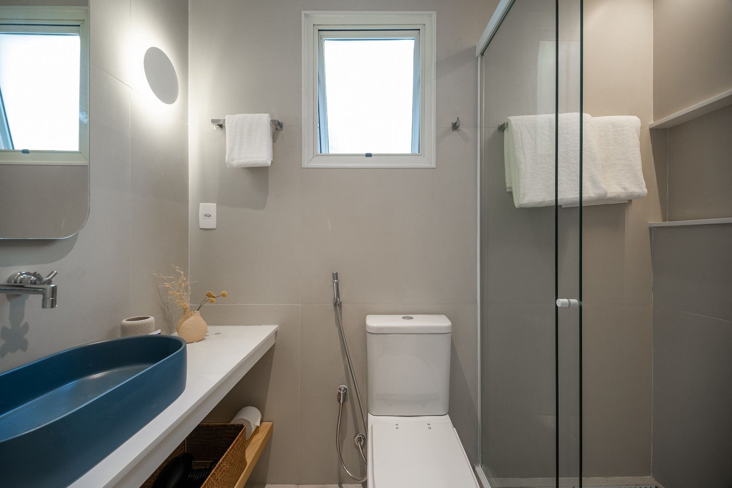 Un baño moderno con un lavamanos azul, un inodoro y una ducha con mampara de vidrio.