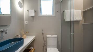 Un baño moderno con un lavamanos azul, un inodoro y una ducha con mampara de vidrio.