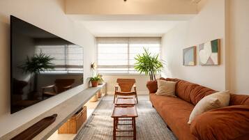 A living room with a large flat-screen TV, a brown sofa, a wooden coffee table, and a potted plant.