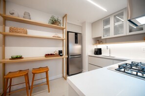 Una cocina moderna con refrigerador de acero inoxidable, estantes de madera, dos taburetes de madera y encimera blanca.