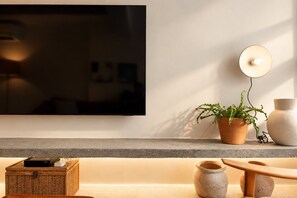 A modern living room with a flat-screen TV mounted on the wall, a potted plant, and a small wooden table with decorative items. - Leblon | 3 Quartos, 2 min da Praia - por Casapē Rio (Rio de Janeiro)