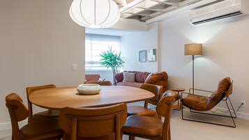 Ein moderner Essbereich mit einem runden Holztisch, sechs Stühlen, einer hängenden Leuchte, einem Topf mit Pflanze, einer Couch mit Kissen und einer Stehlampe.
