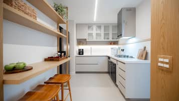 Una cocina compacta con armarios blancos, repisas de madera y un pequeño comedor con taburetes.