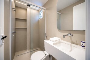 Un baño moderno con ducha envuelta en vidrio, un lavamanos blanco y un inodoro.