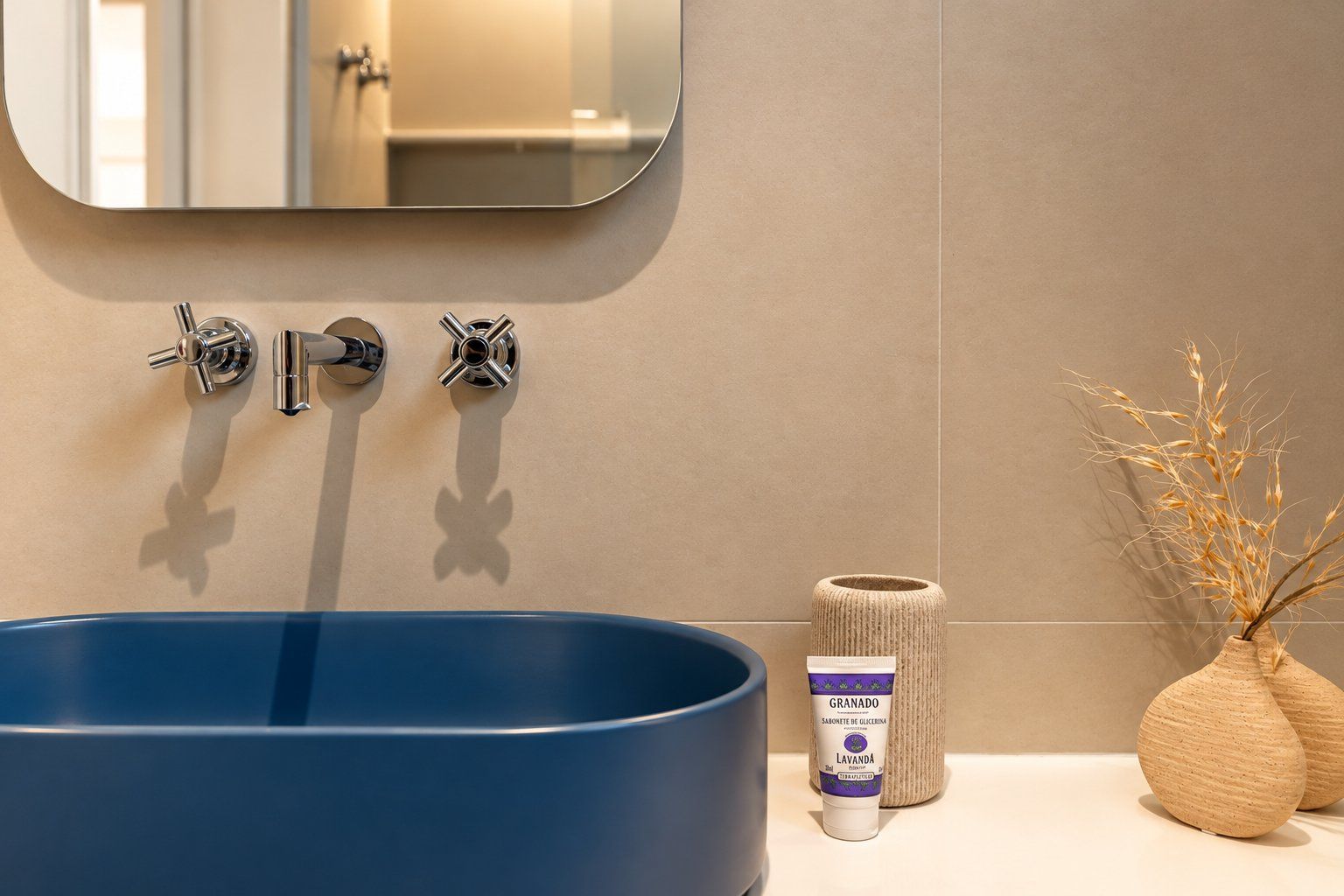 A bathroom with a blue sink, two faucets, a mirror, and a small towel and decorative vase on the counter.