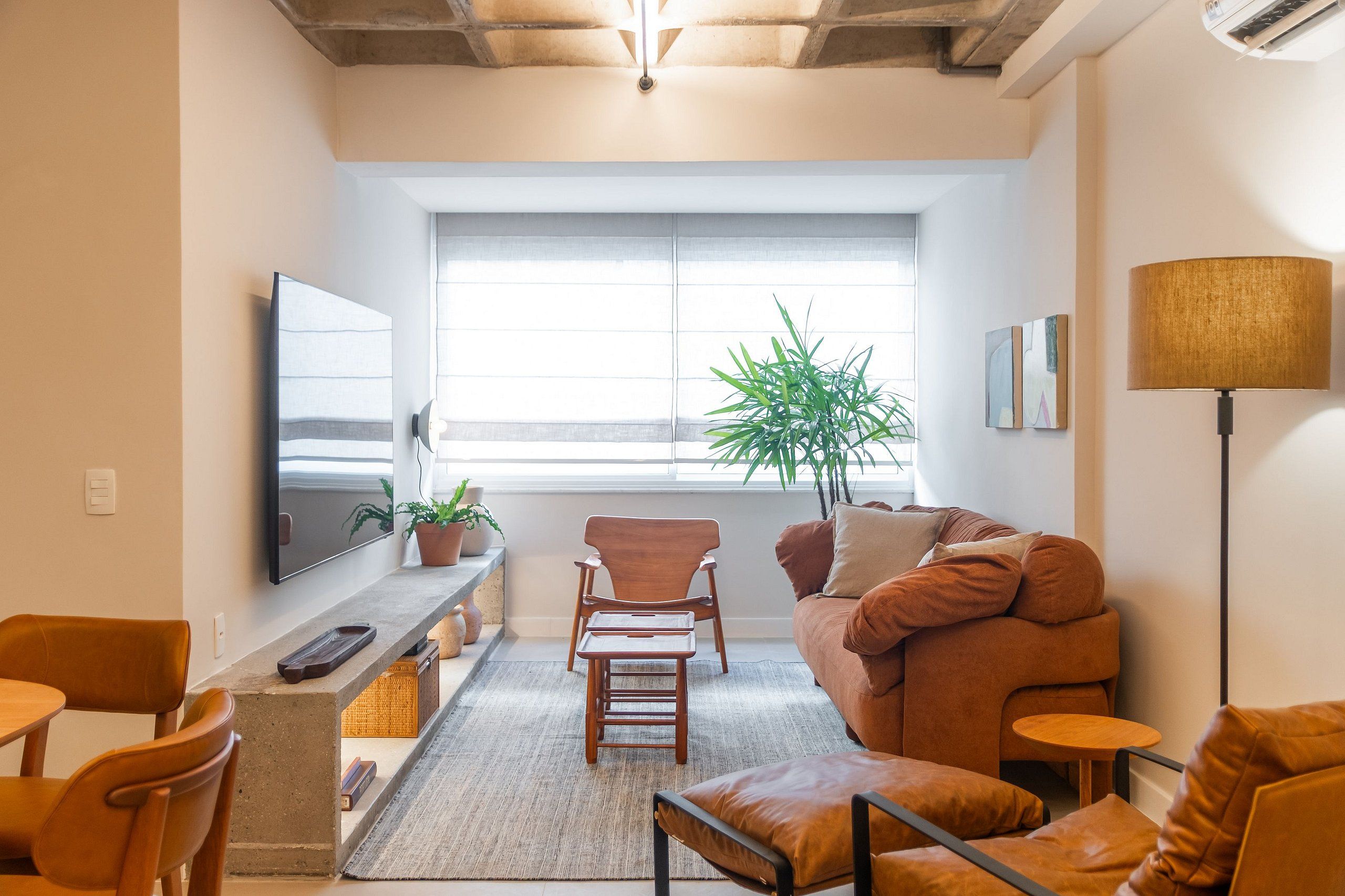 Ein modernes Wohnzimmer mit einer Couch, Sesseln, einem Fernseher, einer Pflanze und einer Lampe.
