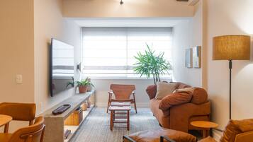 Ein modernes Wohnzimmer mit einer Couch, Sesseln, einem Fernseher, einer Pflanze und einer Lampe.