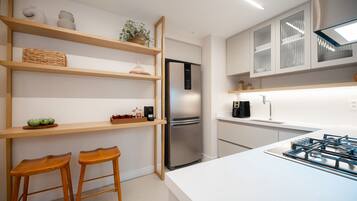 Una cocina moderna con refrigerador de acero inoxidable, estantes de madera, dos taburetes de madera y encimera blanca.
