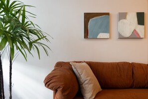 Un canapé marron avec un coussin, une plante en pot et deux tableaux abstraits accrochés au mur.