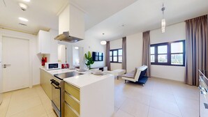 Et moderne køkken med en central ø, et spiseområde med en sofa og store vinduer med gardiner.