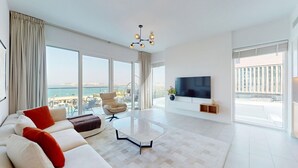 Un saló modern amb un sofà, una taula de centre i una televisió. Hi ha un balcó amb vista al mar.