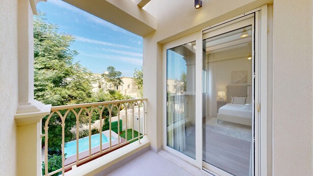 Un balcon avec une piscine, une porte vitrée donnant sur une chambre à coucher équipée d’un lit et d’une table de chevet.