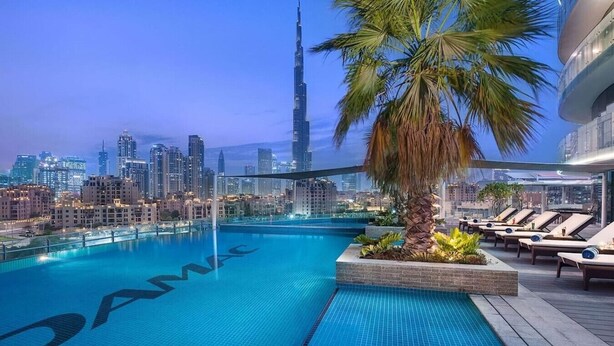 Ein Pool auf dem Dach mit Blick auf den Burj Khalifa, Liegestühle und eine Palme.