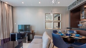 Ein modernes Hotelzimmer mit Essbereich, einer Sitzecke, einem Fernseher und einem Esstisch, gedeckt mit blauen Schalen und Weingläsern.