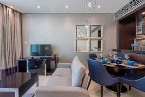 A modern hotel room with a dining area, a sofa, a TV, and a dining table set with blue bowls and wine glasses. - Premium 2 Bed -Iconic Burj Khalifa View I Downtown (Downtown Dubai)