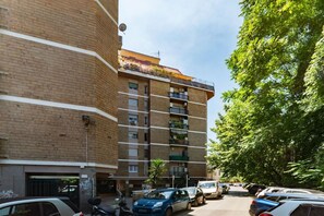 Ein mehrgeschossiges Wohngebäude mit Ziegelaußenwand, Balkonen und einem Parkplatz mit Autos.