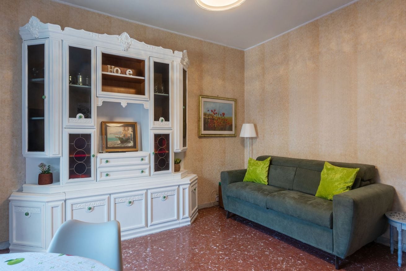Una habitación con un sofá verde, un armario blanco con puertas de cristal, un cuadro enmarcado y una lámpara.