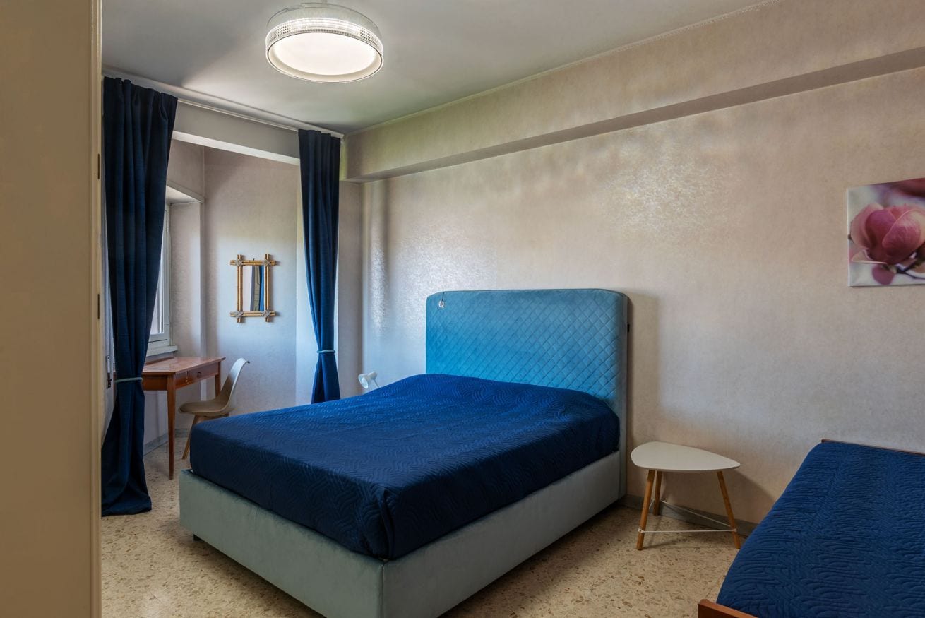 A bedroom with a bed, a small table, a chair, and a wall-mounted mirror.