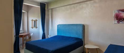 A bedroom with a bed, a small table, a chair, and a wall-mounted mirror.