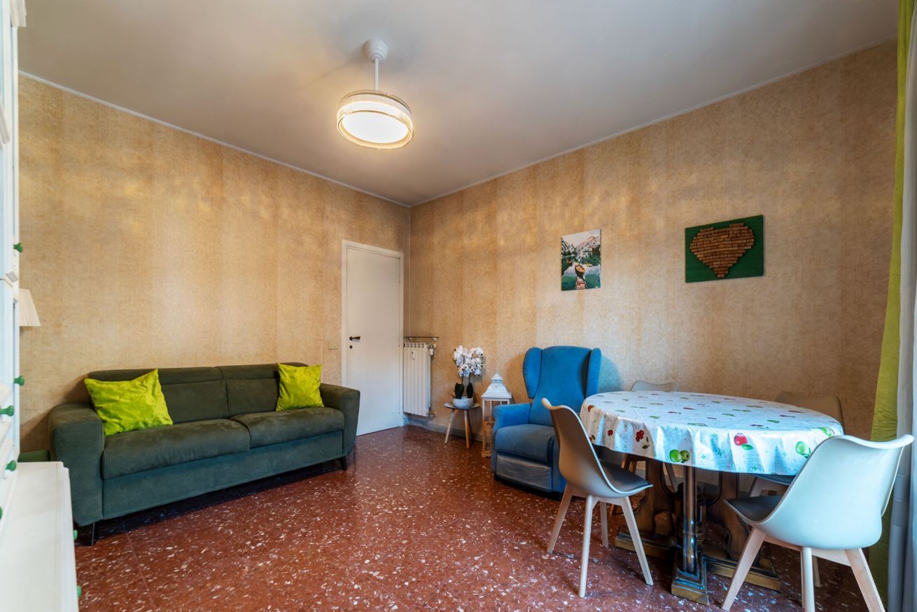 Een kamer met een bank, een eettafel met stoelen, een radiator en een deur.