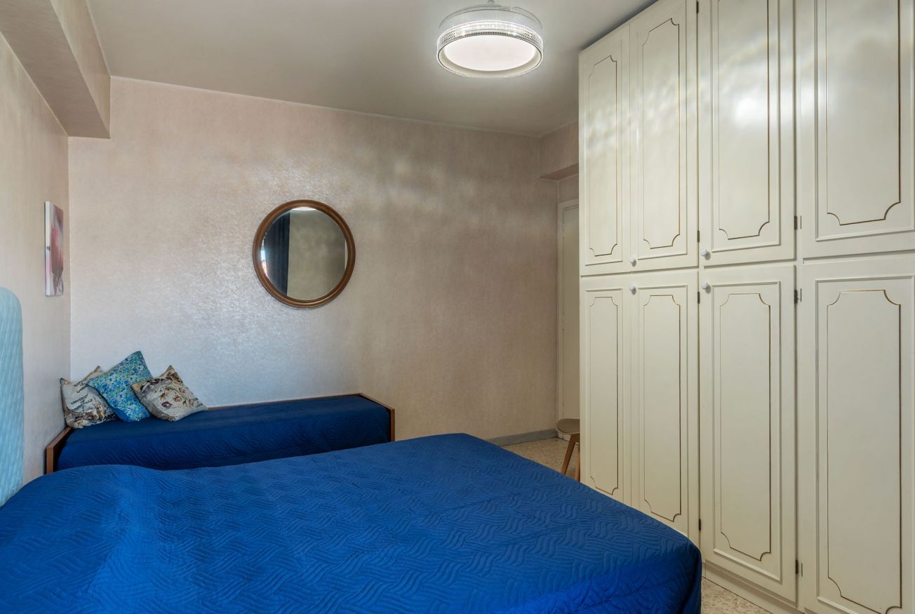 Een slaapkamer met een bed, een kledingkast, een spiegel en een klein krukje.